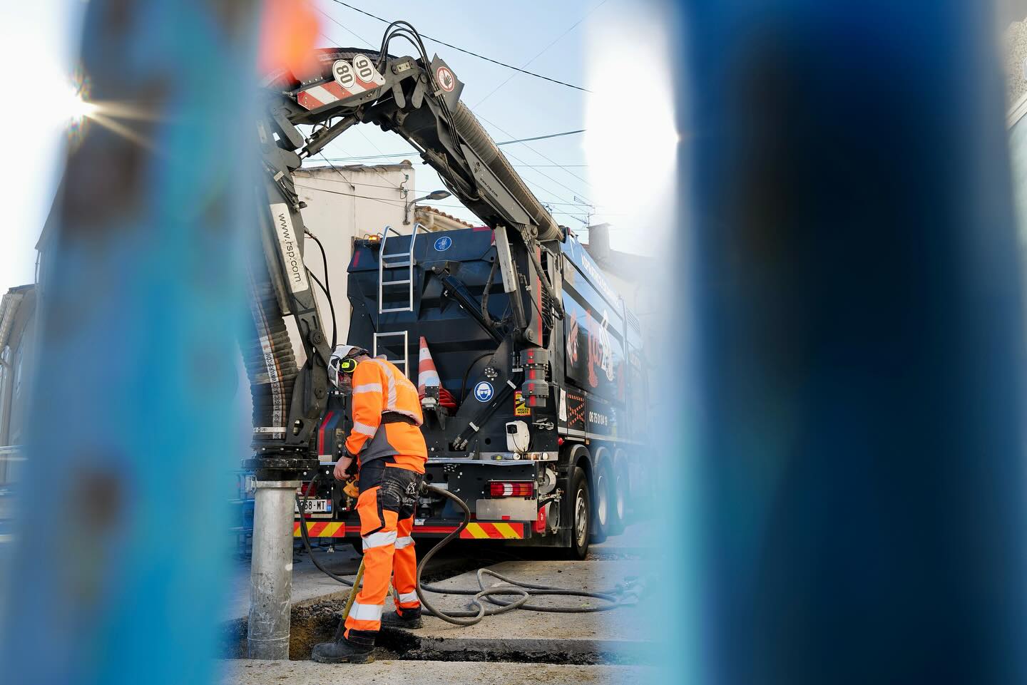 Excavation urbaine sécurisée avec pelle aspiratrice. Ouvrier BTP en tenue orange utilisant un camion d'aspiration puissant pour excavation urbaine. Le bras de la machine porte www.fsp.com.